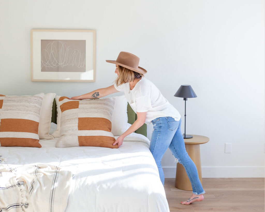 Interior designer setting up a home and arranging pillows on a bed.