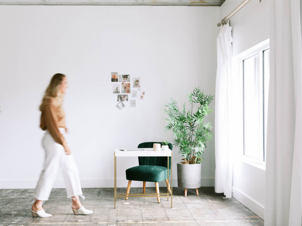 Interior designer walks into minimalistic and stylish office space to sit down at her desk and write her next email newsletter.